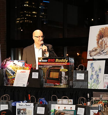 a man speaking during an event with auction items